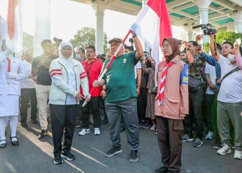 Gubernur Khofifah (kiri) memberikan bendera merah putih pada pimpinan organisasi kemasyarakatan, salah satunya pada Ketua DPW LDII Jawa Timur KH Moch Amrodji Konawi. Dok: LINES.
