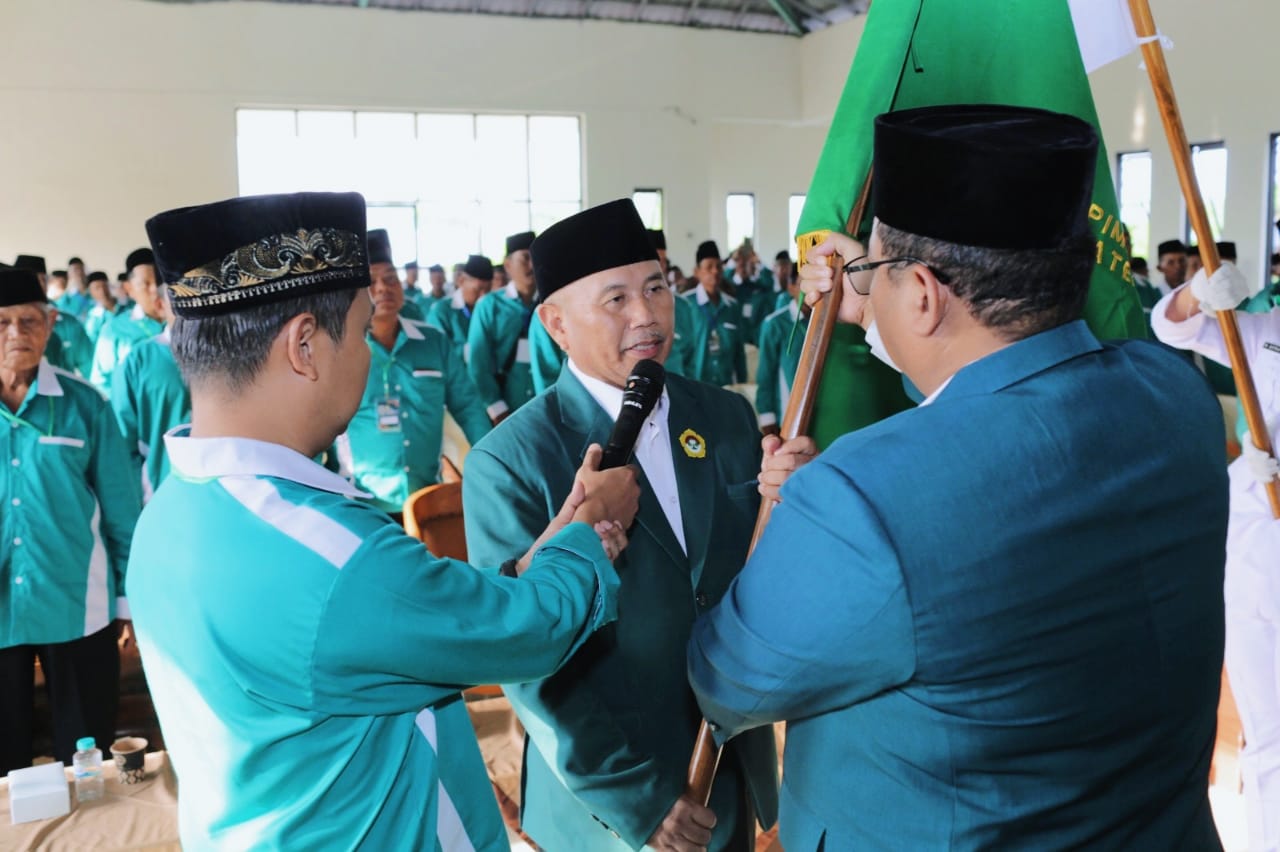 Ketua DPW LDII Jawa Timur, KH Moch. Amrodji Konawi (kanan), menyerahkan panji organisasi kepada Murkani (tengah) usai terpilih kembali sebagai Ketua DPD LDII Kabupaten Nganjuk masa bakti 2025–2030 dalam Musda VIII LDII Nganjuk, Rabu (24/9). Dok: LINES.