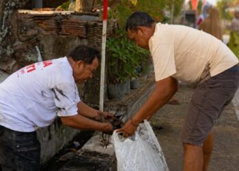 Dua warga LDII Babat bergotong royong membersihkan saluran air di lingkungan permukiman dalam rangka kerja bakti menyambut HUT Ke-81 RI, Sabtu (15/8/2026). Foto: LINES Lamongan
